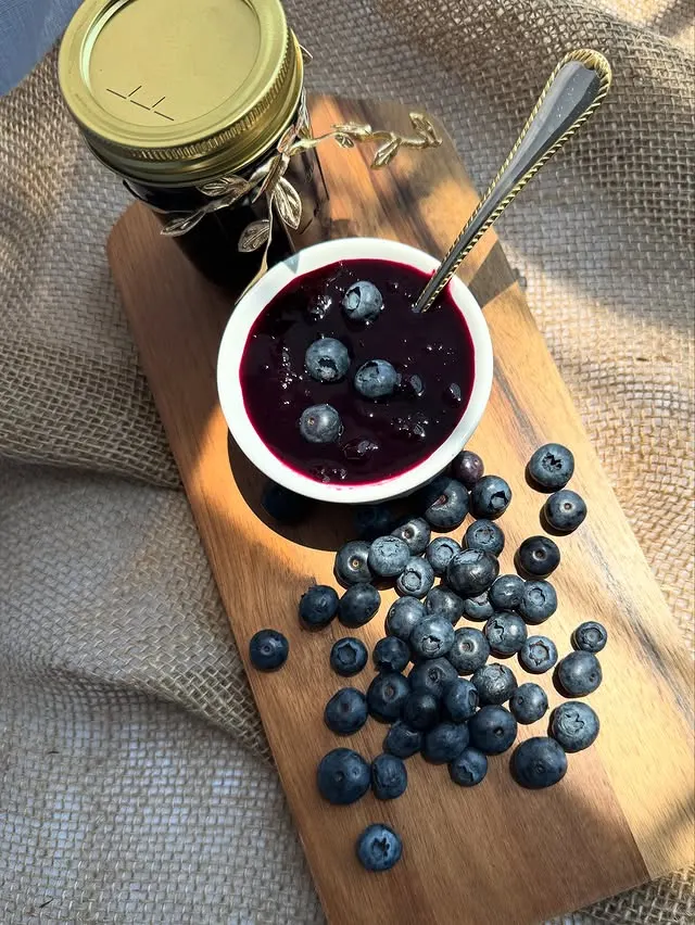 A jar of homemade blueberry jam with berries on a table